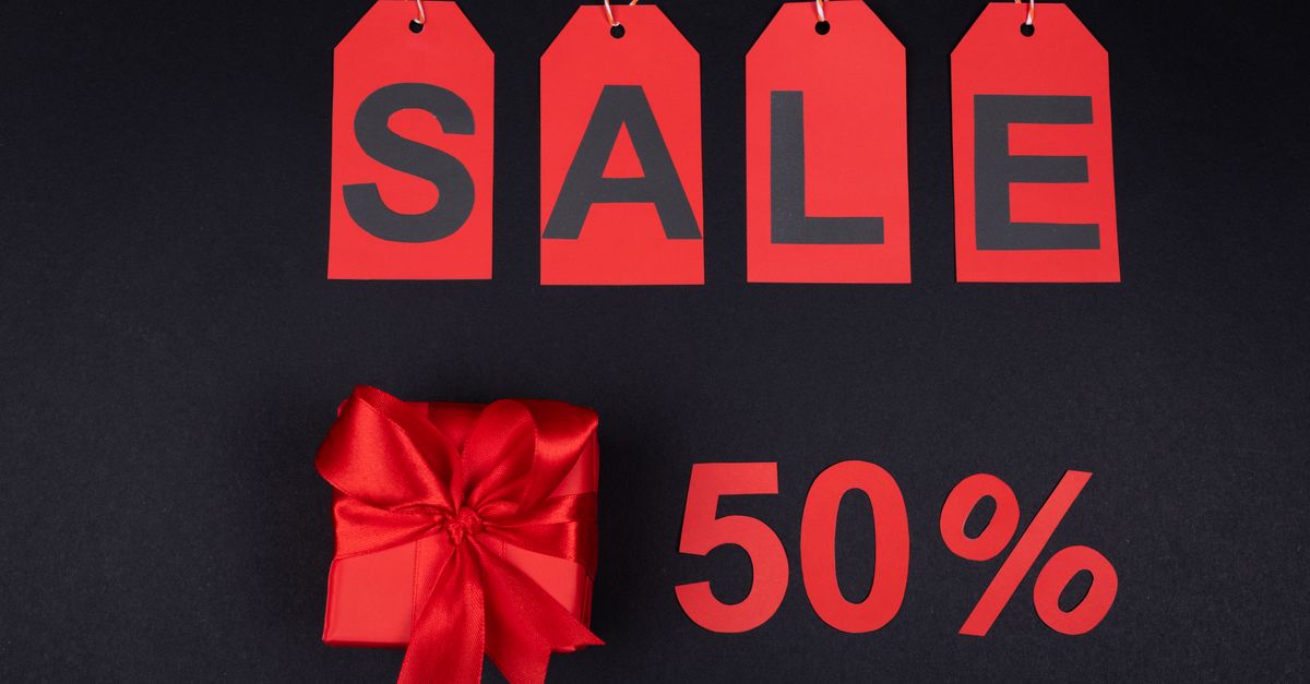 Red gift box next to sale tags and 50% sign on black background, ideal for promotions.